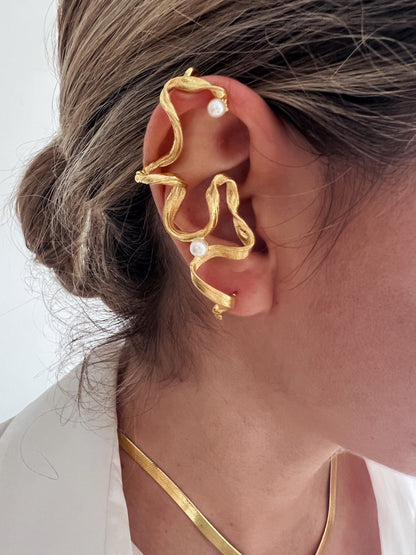 May include: Gold ear cuff with a twisted design and three pearl accents. The cuff is worn on the upper part of the ear.