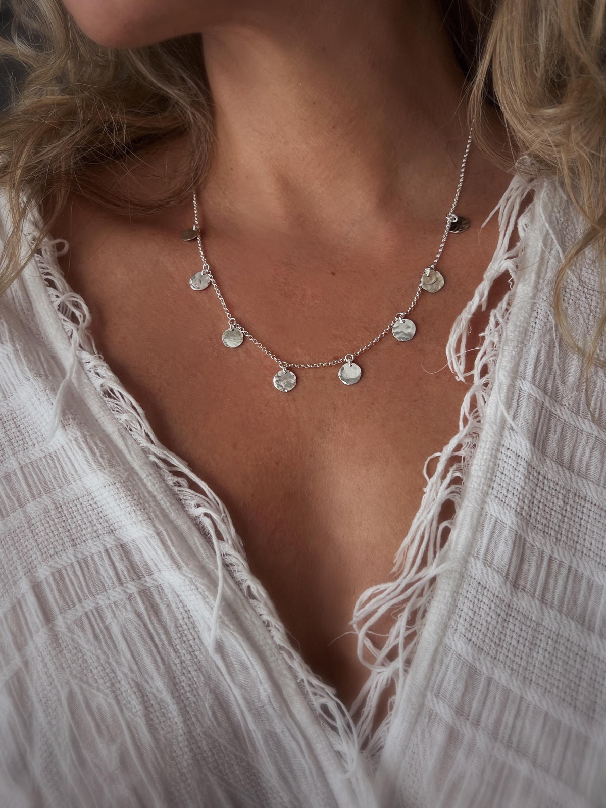 May include: A silver necklace with a delicate chain and multiple small, round, hammered silver charms hanging from it.