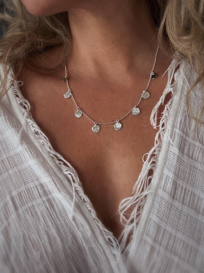 May include: A silver necklace with a delicate chain and multiple small, round, hammered silver charms hanging from it.