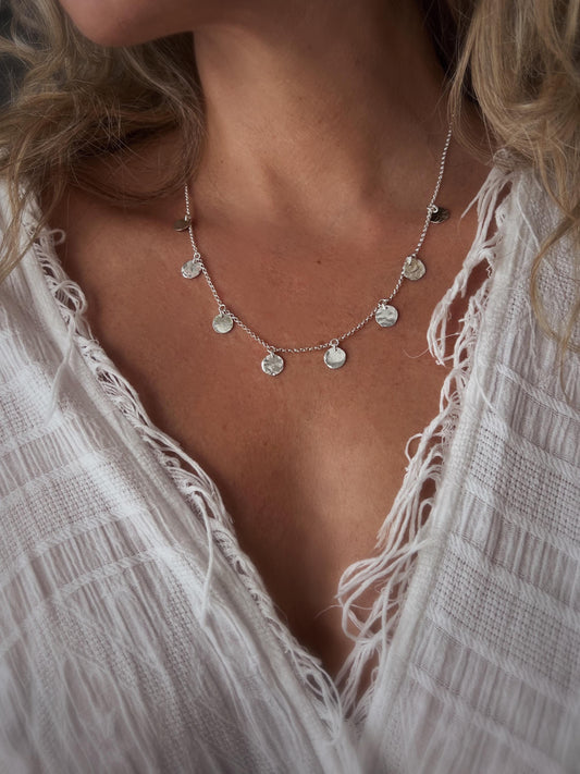May include: A silver necklace with a delicate chain and multiple small, round, hammered silver charms hanging from it.
